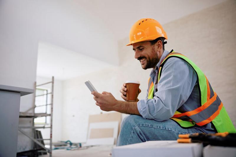 Seated builder updating social media on his phone while on coffee break